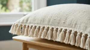 A boho-style cream linen cushion with tassel fringe edges, perfect for adding texture to a budget interior.