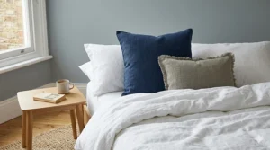 Two navy blue linen pillows under £20 layered on a white duvet for a cosy, minimalist UK bedroom style.