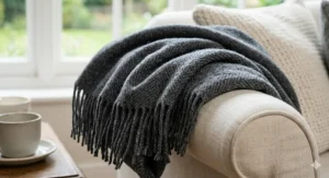 Close-up detail of the soft fringe and intricate herringbone weave of a grey merino wool throw blanket on a sofa arm.