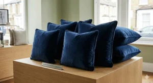 A selection of square and rectangular navy blue velvet cushions in various sizes displayed on an oak plinth.
