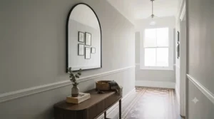 Slim black metal arched mirror hanging above a fluted oak console table in a well-lit hallway with Minton floor tiles.